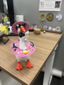 A summer tabletop goose wearing a pink swim ring and sunglasses