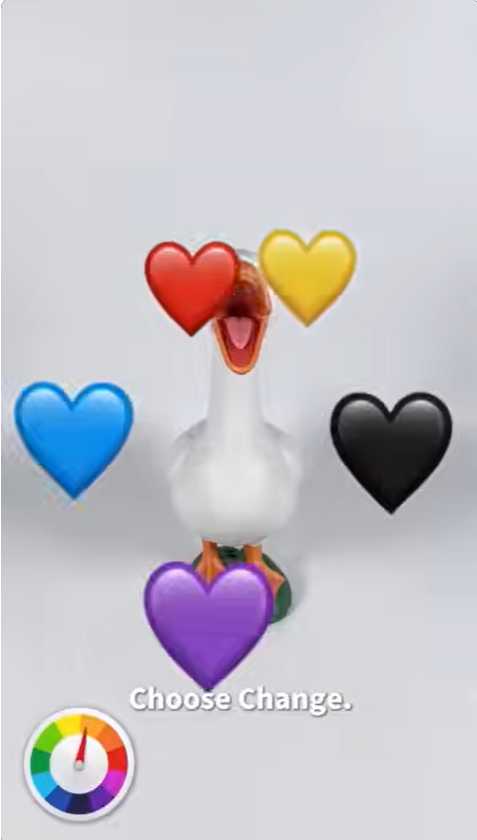 A white toy goose facing forward with its mouth open, surrounded by red, yellow, blue, black, and purple heart emojis